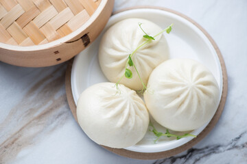 Plastic takeaway plate with freshly cooked chinese baozi, horizontal shot on a white stone background, elevated view