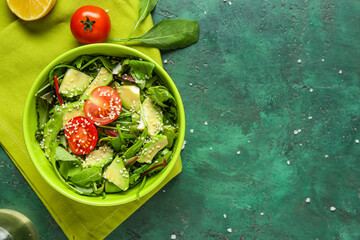 Bowl of tasty avocado salad with cherry tomatoes and sesame seeds on green background