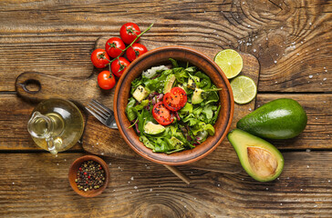 Bowl of tasty avocado salad with cherry tomatoes and lime on wooden background