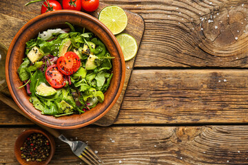 Bowl of tasty avocado salad with cherry tomatoes and lime on wooden background