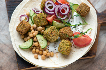 Flat bread with falafel, yogurt, chickpeas and fresh vegetables on a wooden serving board, horizontal shot, closeup