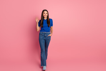 Cheerful young woman in casual attire waving with a warm smile, standing against a vibrant pink...
