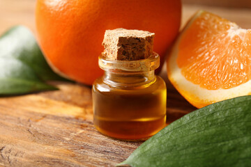 Bottle of orange essential oil with leaves and fresh fruits on wooden background, closeup