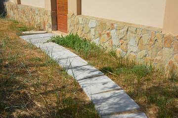 Path to the fence made of concrete blocks. House fence with wild stones foundation and paited wall.