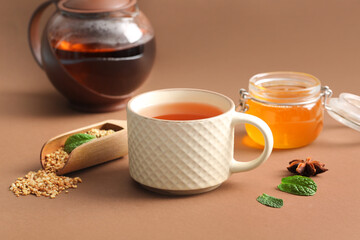 Cup of hot buckwheat tea with mint leaves and wooden scoop on brown background