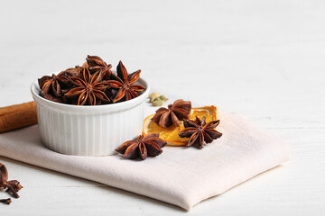 Bowl with anise stars and slice of dried orange on white wooden background