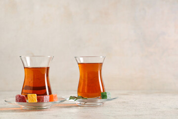 Glasses of Turkish tea with delights and leaves on light background