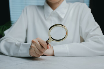 Person holding magnifying glass on white table surface, Business concept
