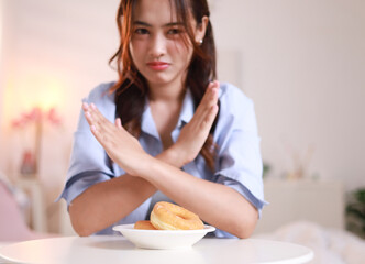 Young woman pushes hand away, rejects sugary donuts, donuts and sweets on plate, weight loss concept, healthy weight loss