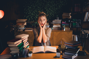 Young woman surprised while studying late at home with books stacked high on her desk in cozy apartment setting
