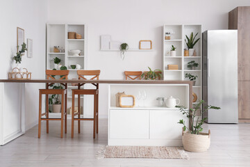 Interior of stylish kitchen with island table, refrigerator and shelving units