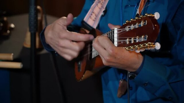 Close-up of a person playing a charango, a small Andean stringed instrument. The focus is on the musician's hands and the instrument