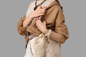 Beautiful young fashionable woman with wicker bag and stylish jewellery on grey background, closeup