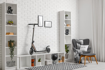 Interior of living room with electric scooter, armchair and shelving units near white brick wall