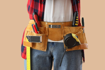 Male construction worker with professional tools on beige background, closeup