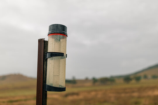Rain gauge on rural farm property measuring rainfall on stormy day