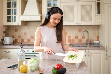 Woman in a kitchen cutting vegetables while wearing headphones. Surrounded by fresh produce, she is calmly focused on her cooking task, enjoying music