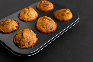 Freshly Baked Muffins in a muffin baking pan on dark background. Breakfast or dessert cupcakes in a muffin tin. Selective focus, copy space