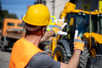 Construction worker directs heavy machinery on a busy site in broad daylight