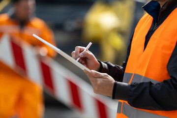 Construction worker in safety vest taking notes at a worksite during daytime