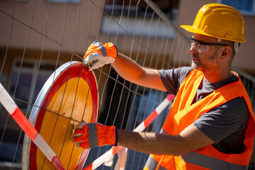 Construction worker installing safety sign near building site during daytime hours