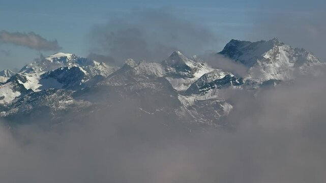 Cinematic aerial shot of snow capped mountain peaks with clouds in front