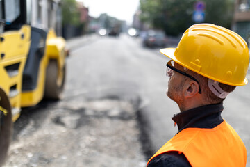 Construction worker observes heavy machinery on a city street during road repair work