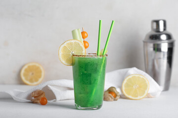 Glass of green bloody mary cocktail garnished with physalis berries and lemon on white background