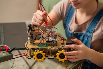 Young individual working on a DIY motorized robot car, testing circuits with a multimeter. Focusing...