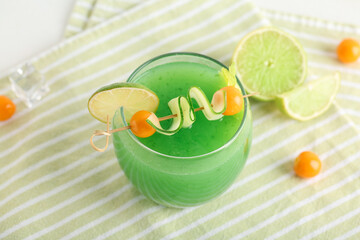 Glass of green bloody mary cocktail garnished with physalis berries, lime and cucumber slice on...