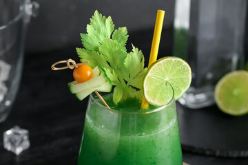 Glass of green bloody mary cocktail garnished with lime, physalis berry and cucumber slice on black...