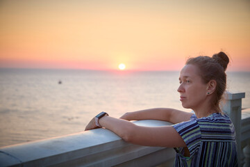 A woman looks thoughtfully at the sunset over the ocean