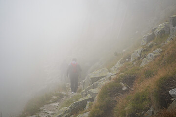 Obraz premium People hiking in a thick fog on top of the mountains on a rocky mountain slope path in High Tatra mountains, Slovakia