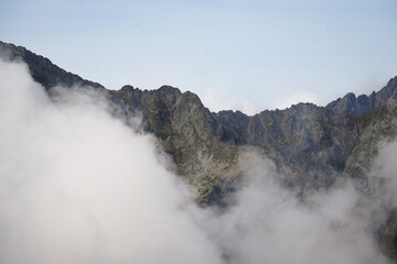 Mountain valley full of clouds and mountain peaks peeking through the clouds with light blue sky background, High Tatra mountains, Slovakia