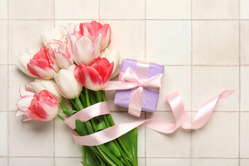 Beautiful tulip flowers and gift box on white tile background. Mother's Day celebration