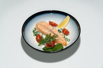 Grilled Salmon Fillet Served with Spinach Cream Sauce, Cherry Tomatoes, Dill, and Lemon Wedge in Ceramic Bowl