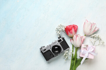 Beautiful tulips with gypsophila flowers, gift box and photo camera on light blue background....