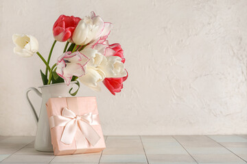 Vase with beautiful tulip flowers and gift box on white tile table. Mother's Day celebration