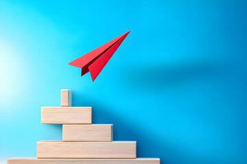 Fototapeta premium A red paper airplane is soaring above wooden blocks against a blue background, symbolizing creativity and innovation in business.