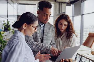 In a modern office environment filled with lush greenery, a dynamic team engages in fruitful collaboration on a laptop