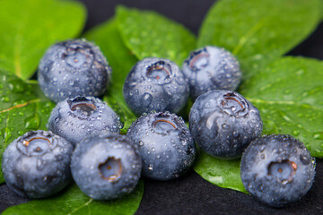Fresh ripe blueberries with green leaves on black background, closeup