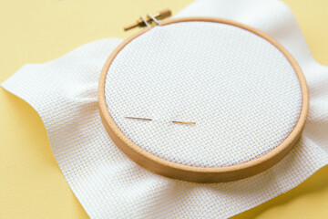 Embroidery hoop with white canvas fabric and needles placed on top, lying on yellow background, ready for stitching, concept of handicraft © Evgeniia Primavera