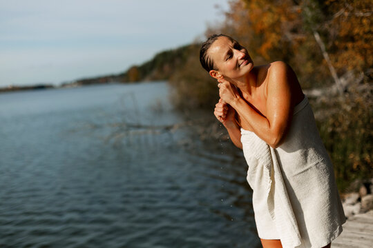 Mid adult woman wringing wet hair while wearing towel at lakeshore