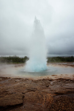Strokkur geyser erupting hot water and steam against sky in Iceland
