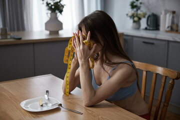 Depressed anorexic slim woman with measuring tape sitting at dining table