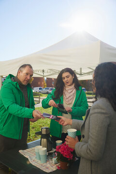 Male and female charity owners giving flyers to woman in park at sunny day