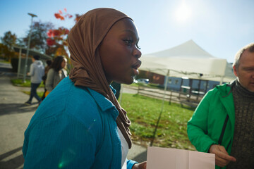 Woman wearing headscarf holding talking with charity volunteers in park at sunny day