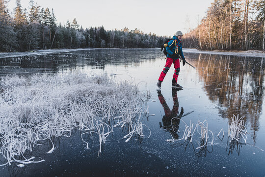 Woman ice skater skating on frozen lake amidst forest during winter