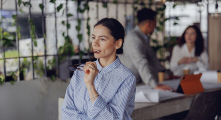 A highly focused businesswoman takes a moment to reflect in her stylish, plantfilled office...