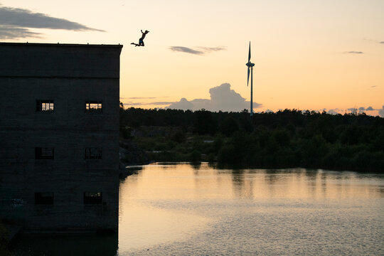 Unrecognizable person jumping from top of building in water at sunset